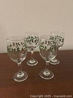 Four clear glass wine glasses with holly and berries decoration around the bowl, made for Christmas.
