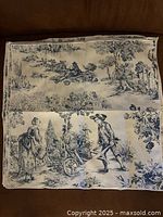 Eight cloth napkins stacked showing blue and white printed farm scenes with figures and rural motifs.