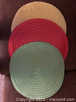 Photo showing three colorful round woven placements in yellow, red, and green colors stacked with red on top, cream/yellow in the middle, and green on the bottom.