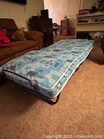 Foldaway bed fully opened showing the mattress and metal frame on carpeted floor in living room.