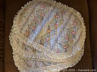 Photo showing 6 oval placemats stacked, featuring a pastel floral pattern and cream ruffled lace edges.