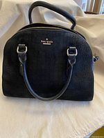 Front view of black embossed crocodile texture leather handbag with dual handles and Kate Spade New York gold logo plaque