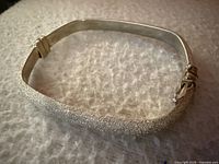 Top angle close-up of the rectangular textured silver bracelet showing the shimmering finish and part of the clasp.