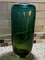 Front angle of a tall, heavy glass vase with a greenish-blue to amber gradient and etched square geometric pattern on the body.