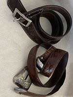 Coiled Roots dark brown leather belt with silver-tone square buckle and detailed stitching.