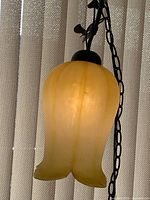 Front view of vintage yellow frosted glass tulip hanging lamp illuminated, showing soft glow and shape