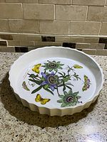 Full view of round Portmeirion ceramic baking dish with colorful botanical illustrations of blue passion flowers and yellow butterflies.