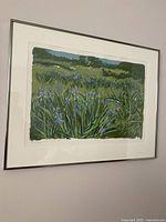 Framed vintage print hanging on wall showing field of grass and blue flowers