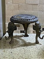 View of full metal stand showing round top with carved decorative pattern and three detailed elephant legs.