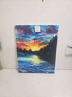 Front view of the painted canvas artwork showing nature, water, and sunset scene with vibrant colors.