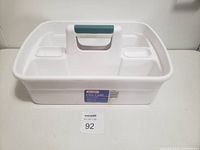 Front-facing photo of white Rubbermaid Ultra Caddy bucket. The caddy has a central handle, dual compartments on each side, and is empty.