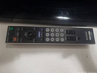 Sony remote control with numeric keypad, volume and channel buttons shown flat on white background.