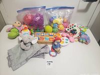 Photo showing assortment of baby toys including soft plush animals, bags of textured plastic balls, wooden blocks, and various rattles and teething toys.