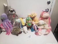 Wide shot overview of all plush toys arranged on white surface against door background.