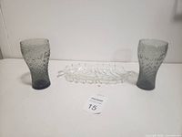 Two black Coca-Cola glasses and clear glass dish displayed against plain background with auction lot tag.