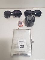 Lot contents including photo album, two women's sunglasses, small deck of playing cards, and small black plastic pot