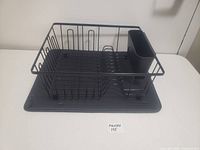 Photo showing angled view of black metal dish rack with utensil holder and drip tray on white surface.