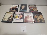 Photo of 8 DVDs and VHS movies arranged on flat surface showing front covers and providing visual condition of each item.