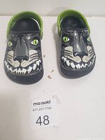Front view of kids Crocs showing panther face design and green heel straps.