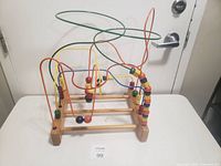 Wooden bead maze toy with colorful beads on twisted metal wires and wooden base placed against a white door.