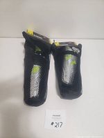 Two Under Armour kids soccer shin guards in black mesh carrying pouches with visible yellow and black tag packaging.