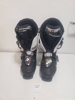 Front view of the men's Salomon ski boots in black and white, showing the size label and adjustable buckle on the front of each boot.