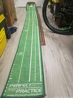 Photo showing the length and green turf of the mini golf putting green with "Perfect Practice" branding and distance markers up to 8 feet.