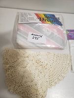 Twin sheet set in plastic package labeled 'marcoid 245', crocheted doily, and packaged washing machine bags on white surface.