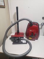 Red SEBO canister vacuum with hose, wand, floor head and tool attachments