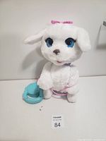 Full front view of the white plush walking dog toy with blue eyes, pink bow, pink trim, and accompanying blue remote control.