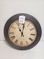 Front view of the vintage style round wall clock showing Roman numerals and black frame.