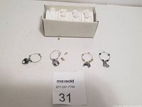 Four metal wine glass charms laid out with small decorative elements, next to a box of white floral bracelet bands