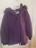Front view of the purple women's winter coat hung on a white hanger showing front button closure, side pockets, and ribbed cuffs on sleeves.