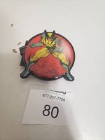 Front of the Wolverine belt buckle showing Wolverine in his yellow and blue costume with claws extended against a red background.