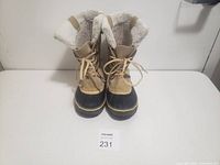 Front view of women's winter boots with beige uppers and black rubber soles, showing sherpa fleece lining inside and laces tied in front.
