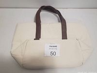 Photo shows a cream/off-white women's swim carrier bag with brown shoulder straps laid flat against a white backdrop with a MaxSold label '50' attached to it.