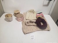 Photo showing three knitted women's items including a chunky knit scarf, knit hat, hair scrunchie, and a multi-colored knit accessory alongside three scented candles.