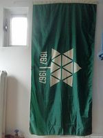 Full view of green vintage Canada Centennial flag with white 1867-1967 centennial logo hung vertically.
