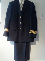 Front view of navy pilot jacket showing gold rank stripes on sleeves and gold buttons, against white wall background.