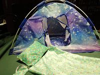 Tent with galaxy pattern and open window flaps, sleeping bag, pillow, and eye mask displayed on a surface