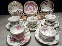Overall set of 8 teacups and saucers arranged showing varied floral and gold designs on fine bone china cups and matching saucers