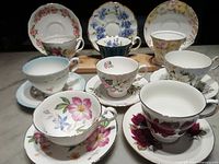 Top-down view showing all eight teacups with matching saucers, arranged in two rows, highlighting the variety of floral patterns and styles.
