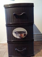 Front view of dark brown resin storage tower with three wicker-textured drawers and handles, with label on middle drawer.