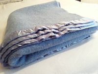 Folded light blue virgin wool blanket with satin edging visible, showing texture and thickness.