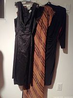 Three dresses hung on wall - vintage Laundry by Shelli Segal black and gold geometric pattern, black satin sleeveless dress, and black long sleeve ruched dress