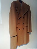 Front view of men's camel-colored double-breasted Aquascutum wool overcoat hanging isolated.