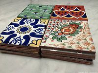 Photo of stacked Talavera tiles showing varied colorful hand painted designs from blue and yellow floral to green and orange patterns.