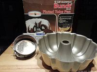 Bundt 12-cup aluminum fluted tube pan with original box and Wilton springform pan placed on wooden surface.