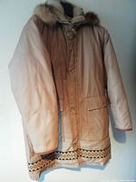 Full front view of beige down insulated parka with fur hood and decorative hem trim.