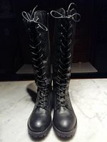 Front view of both tall black lace-up boots side by side on a marble surface under indoor lighting.